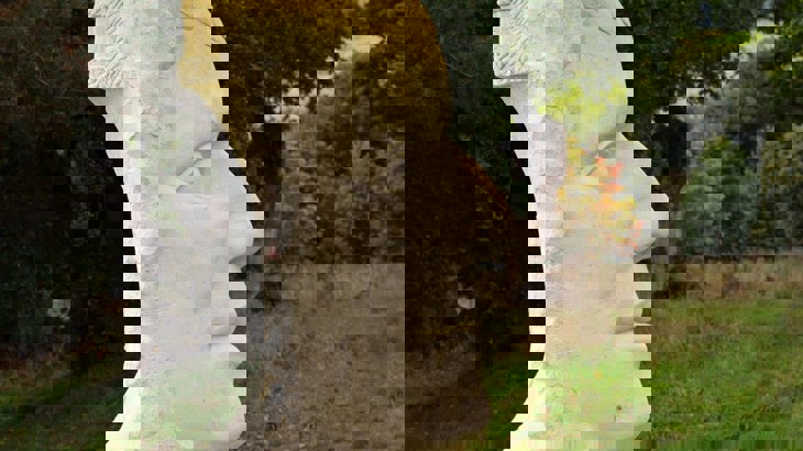 White stone sculpture of a face with grass and trees in the background