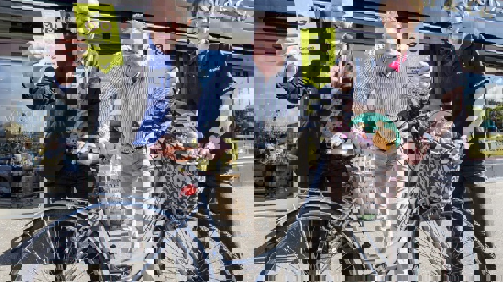 Three people posing with a bike outside a shop with flyers in hand Pedal Perks launch in Northern Ireland