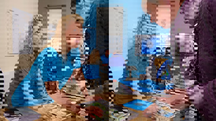 Woman in blue polo shirt showing leaflets to woman in purple jacket over counter