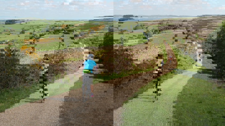 Cyclist in blue jersey following group of other cyclists on gravel path through countryside