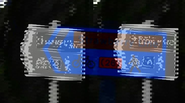 Blue directional sign on pole with bracketed number 26, picture of bike and walker, and title "Strawberry Line"