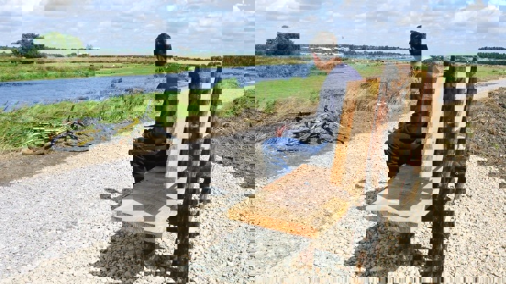 Person sitting on wooden bench by gravel path overlooking river