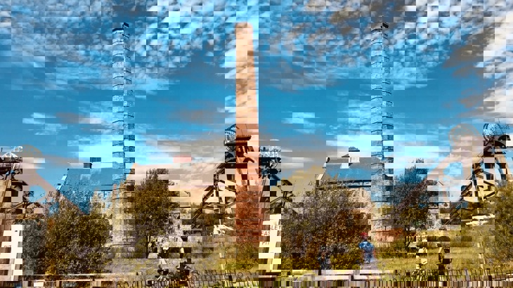 Two children with bikes and cycling gear looking toward old mine building with chimney stack 