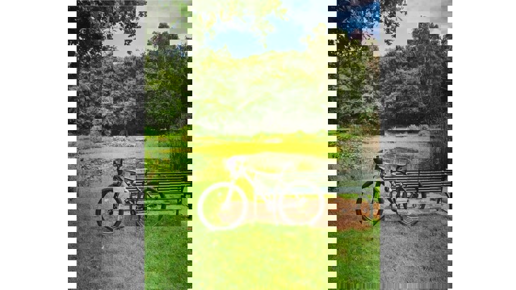 Bike with peaked cap on handle bar leaning up against park bench overlooking pond