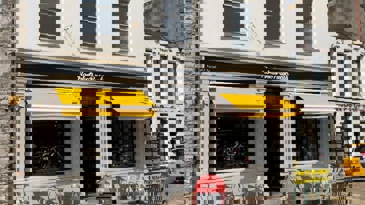Facade of cafe with yellow outdoor shades over the windows and a bike in one of the windows