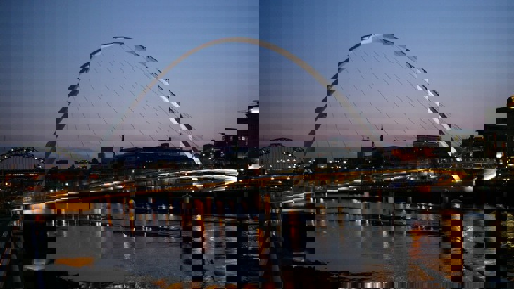 Modern pedestrian bridge with lights underneath, over river in city at night