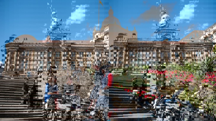 A group of people sit outside Birmingham Council building on a sunny day