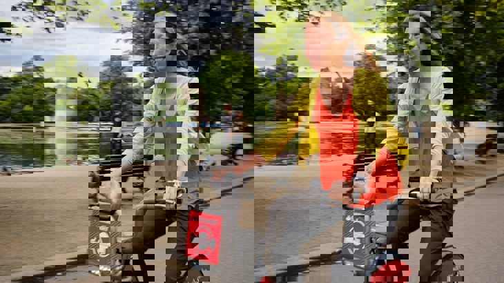 Woman cycles past Victoria Park in Hackney on a city hire bike.