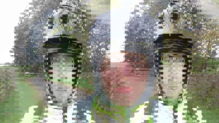 Man wearing glasses, hood, black cycling helmet and high-vis jacket on cycle path