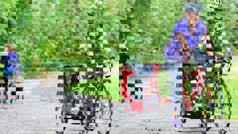 Woman cycling on cycle path pulling small child in trailer