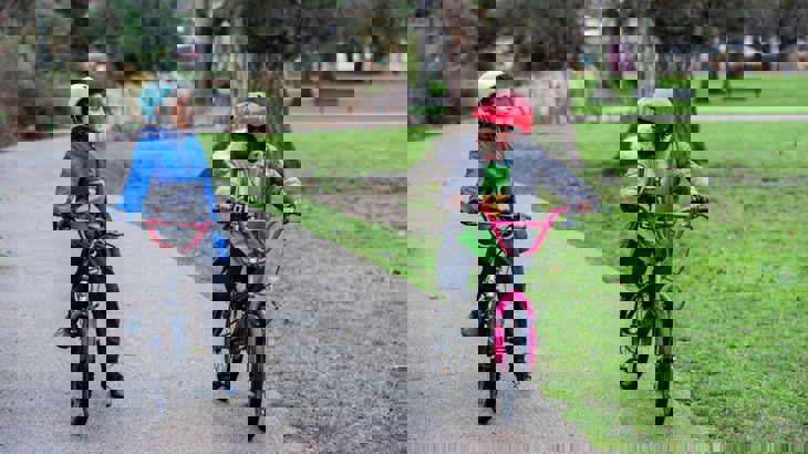 two young children on their bikes with helmets on a traffic-free path