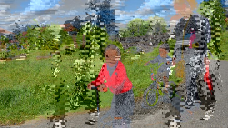 Girl on scooter, boy on bike and mum walking to school along a traffic-free path