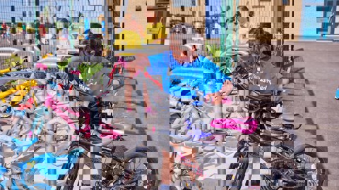 A girl in a blue t-shirt locking her bike to a Sheffield cycle stand in the school playground