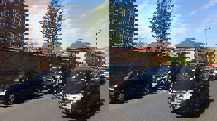 Adult and child holding hands trying to cross the street outside school with lots of cars driving down the road