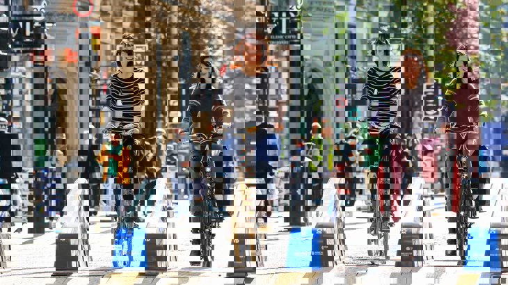 Two women smiling and chatting as they cycle together along a new temporary cycle lane through the high street.