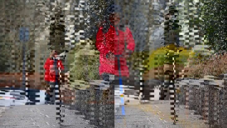A young girl in school uniform, a winter coat and a helmet rides her scooter.