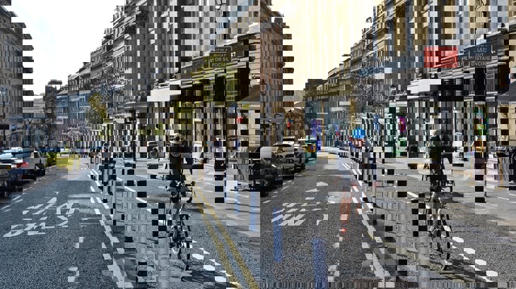 A man wearing a cycle helmet riding uphill along a segregated cycle lane through a city centre.