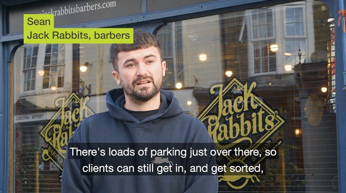 Video thumbnail of a man wearing a navy hoody talking to camera outside his barbershop business.