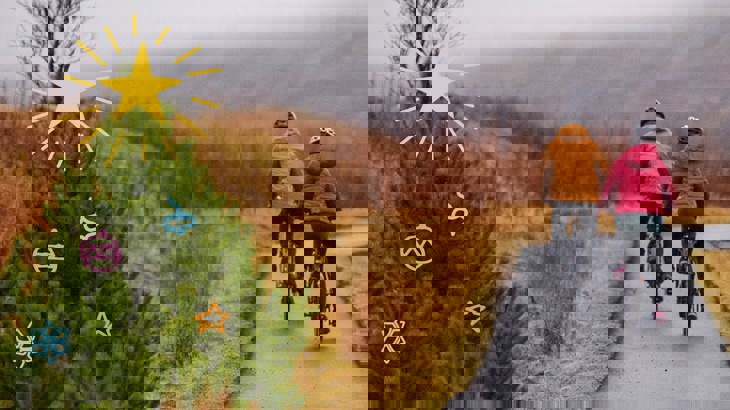 Two people cycling on a traffic-free path past a Christmas tree with illustrated decorations