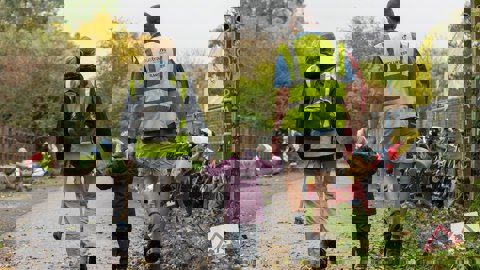 Mum and dad holding hands with their small daughter, wearing Walk Wheel Cycle Trust volunteer high-vis jackets and walking away from camera down a traffic-free route.