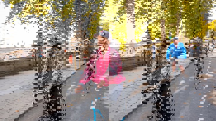 A girl cycles along a segregated cycle lane during the autumn time through Embankment in London, with other people cycling behind her in the background.