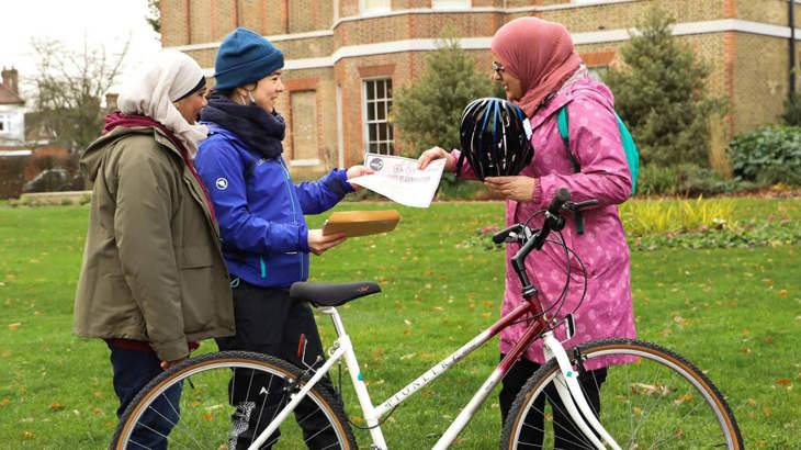 Saika dressed in a pink coat and headscarf, receiving a certificate from a Walk Wheel Cycle Trust officer, standing in front of Saika's new bike.