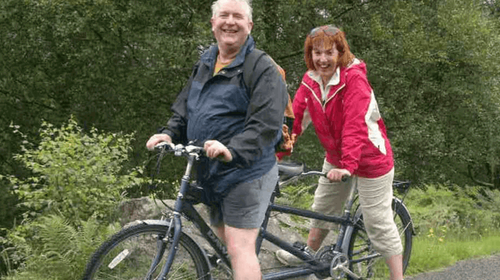 Colin and Diane riding on a tandem bike together, smiling