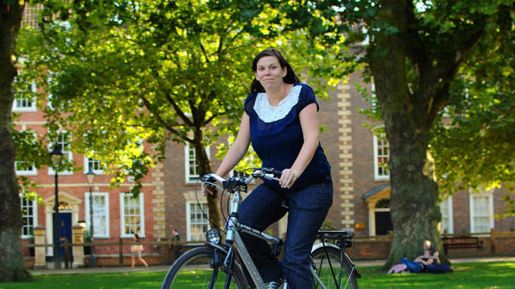 Pregnant lady riding a bike through a city park surrounded by green trees