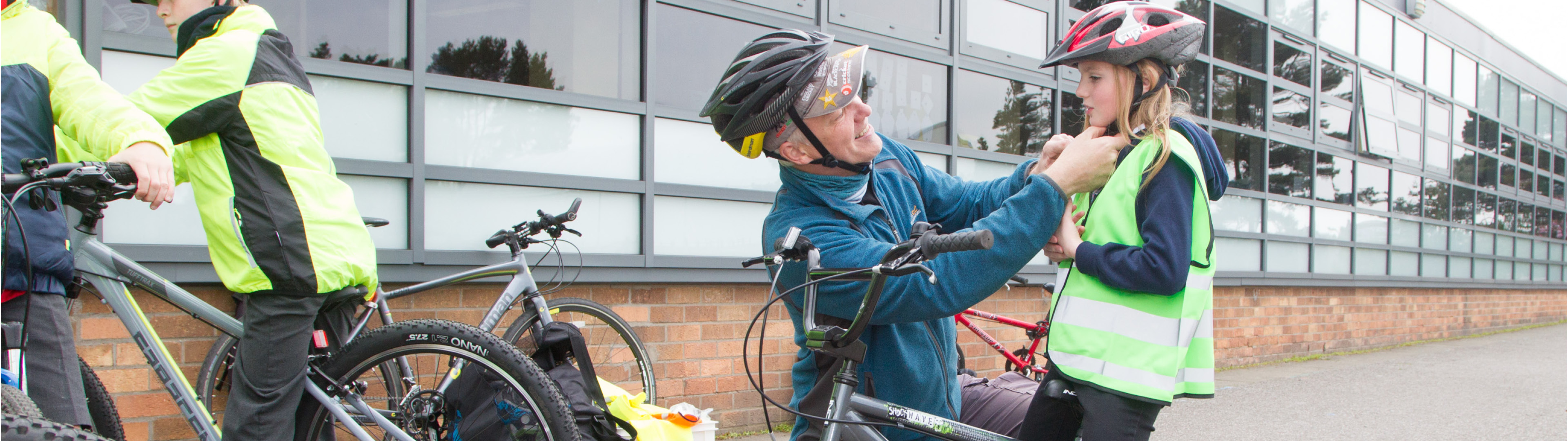 Walk Wheel Cycle Trust schools officer fitting a child's helmet and she stands with her bike.