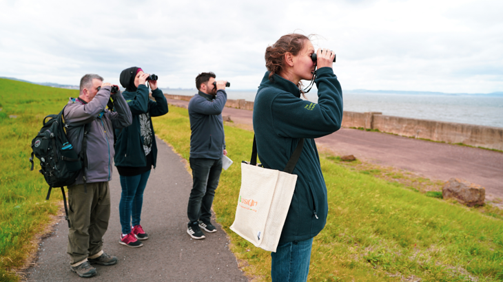 A birdwatching group looks out to sea with their binoculars