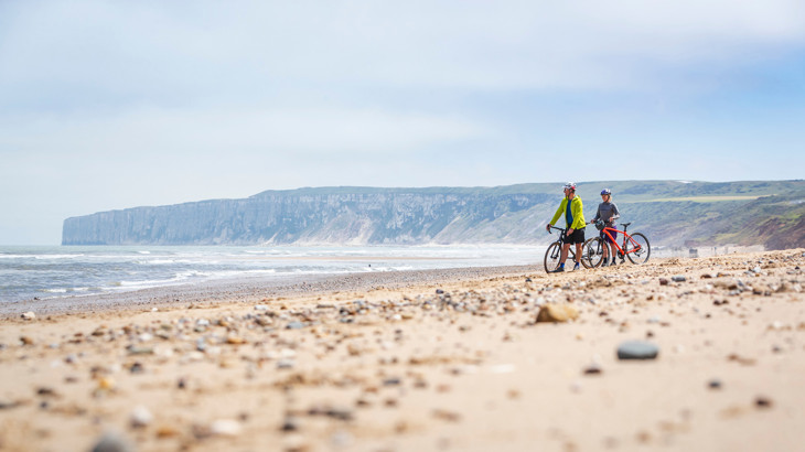 Two people standing with cycles on a beach