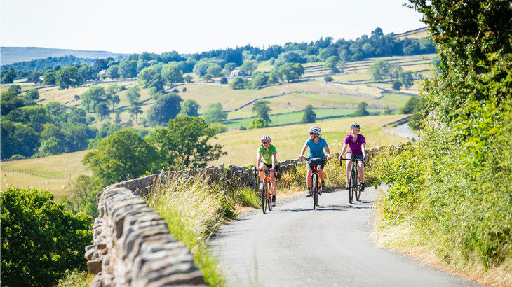 Three people cycling along a traffic-free route with hills in the background