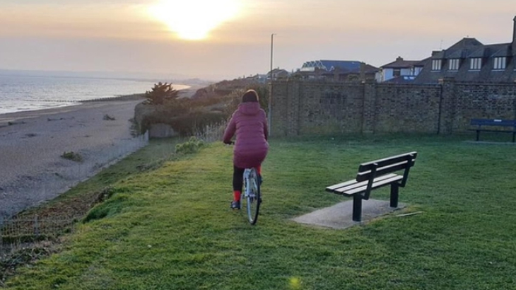 Person cycling into sunset by coast