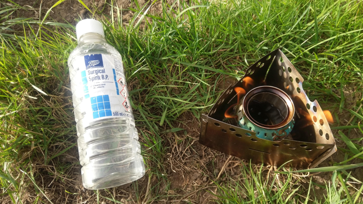 Beer can stove on grass beside bottle of surgical spirit.