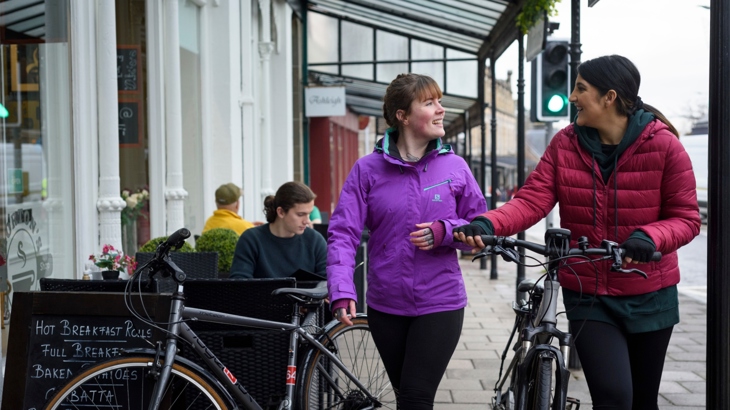 Two women walking and talking with bikes in winter