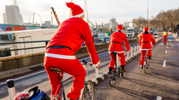 A group of people dressed as Santa cycling in London on a bright day