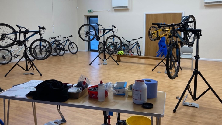 Multiple bikes in maintenance stands in a school hall.