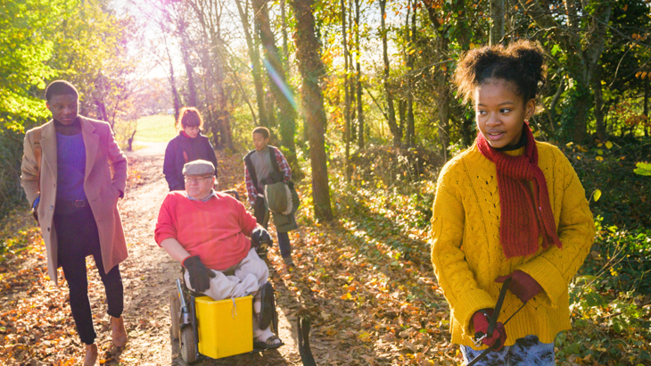 A group of people of different ages walking through a bright woodland on a sunny day 