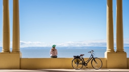 A woman sits on Barry Island promenade looking away from the camera toward the sea. Beside her is a parked e-bike.