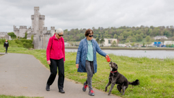 Two women walking with dog in front of Blackrock Castle, Cork.