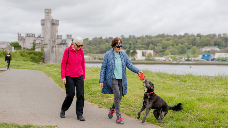 Two women walking with dog in front of Blackrock Castle, Cork.