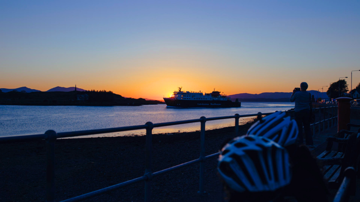 View of sun setting over a ferry crossing a narrow waterway on the Caledonia Way.
