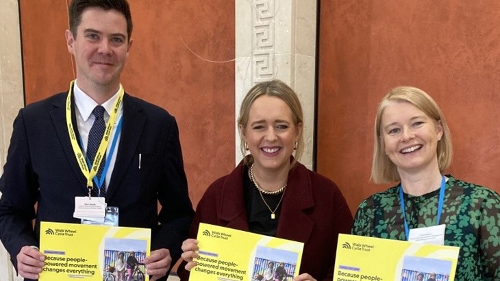 Three people holding yellow booklets at formal event