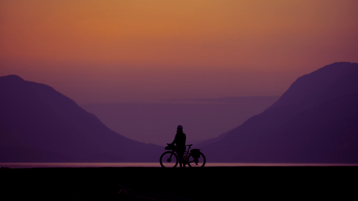 A cyclist looking at the sun setting over the distant mountains.