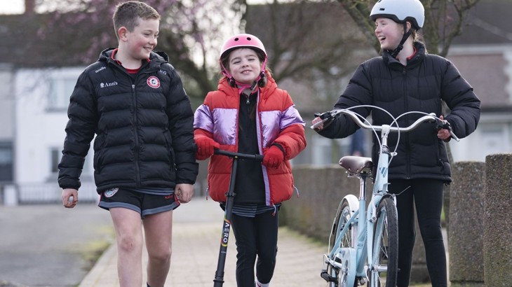 A boy and two girls walk, scoot and cycle together to school