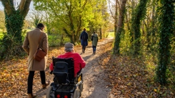 A group of people on a path, the festival way on a sunny autumn day. 3 people are walking and one person is wheeling.