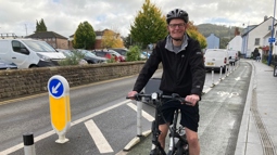 Abergavenny resident Daniel riding a black e-bike in a bike lane, smiling at the camera