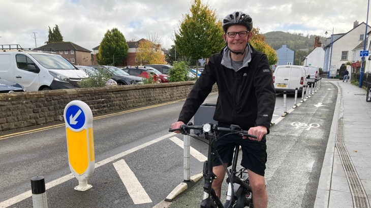 Abergavenny resident Daniel riding a black e-bike in a bike lane, smiling at the camera