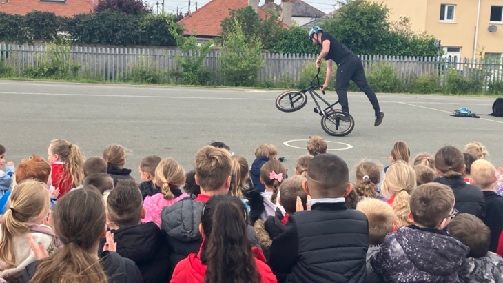 Pupils sit on a playground watching a BMX show.